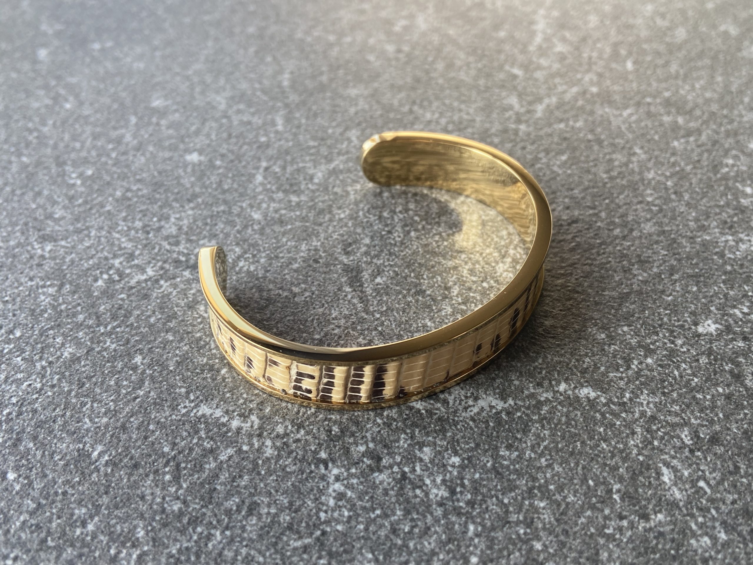 Gold-plated stainless steel cuff bracelet with Sand Scale Line leather inlay on stone background