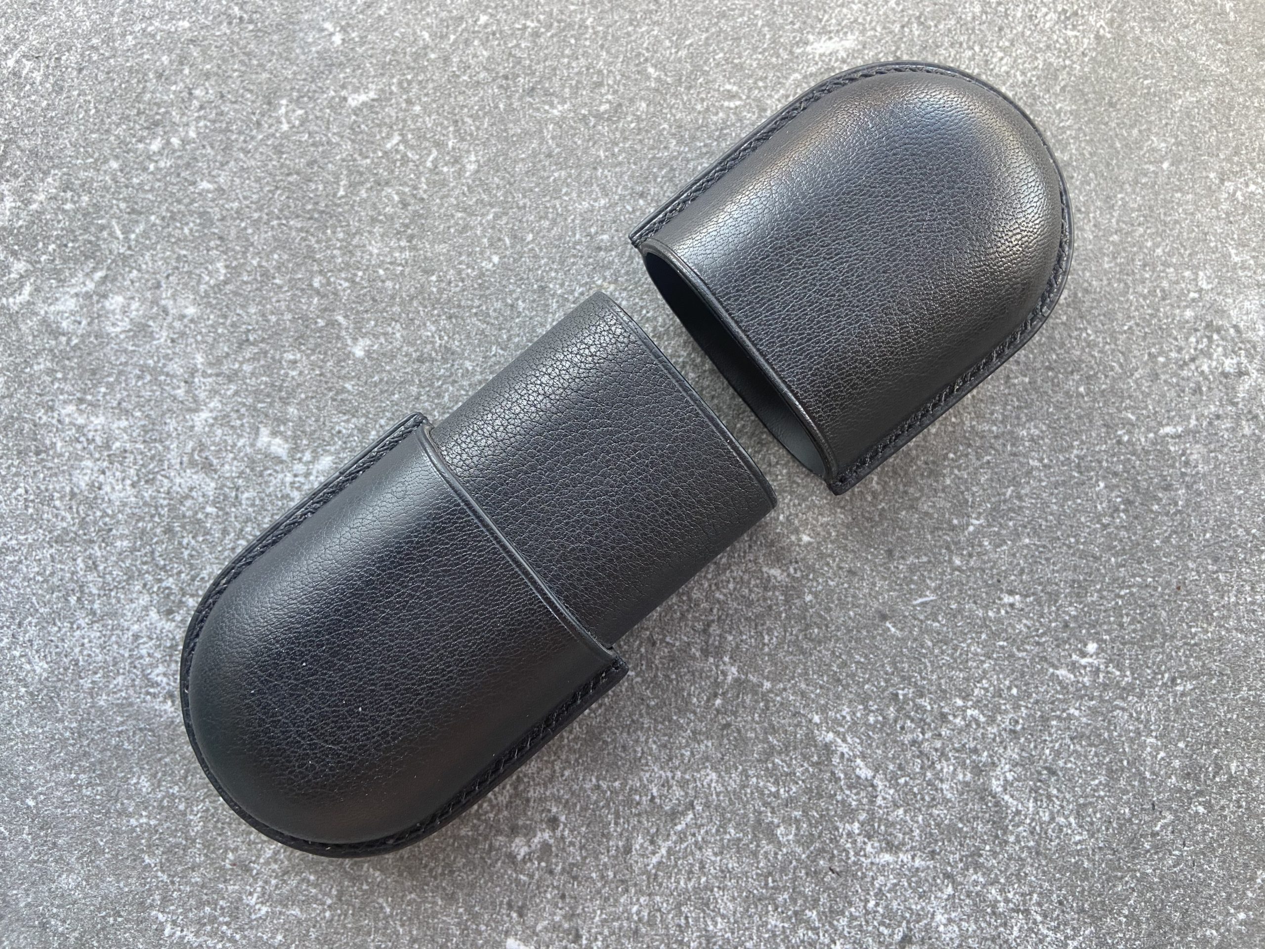 Leather glasses case with sliding lid in black leather shown open in two parts on a stone surface