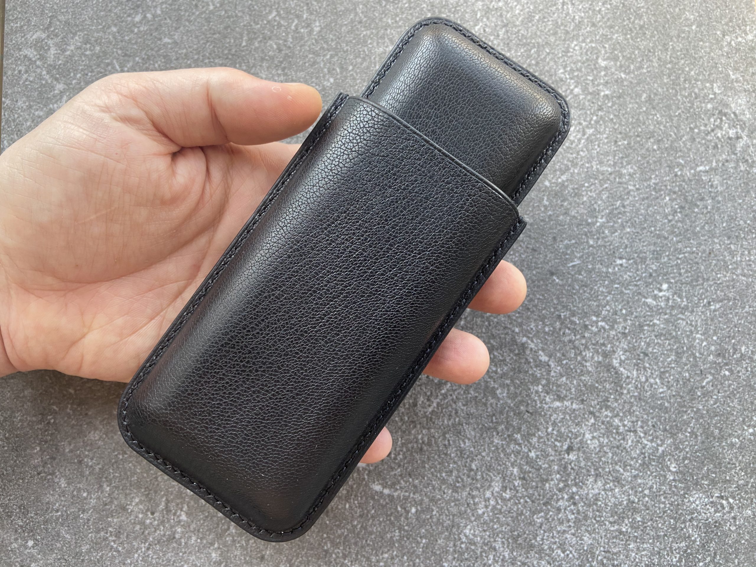 Leather cigar case in black leather held in hand on a stone surface