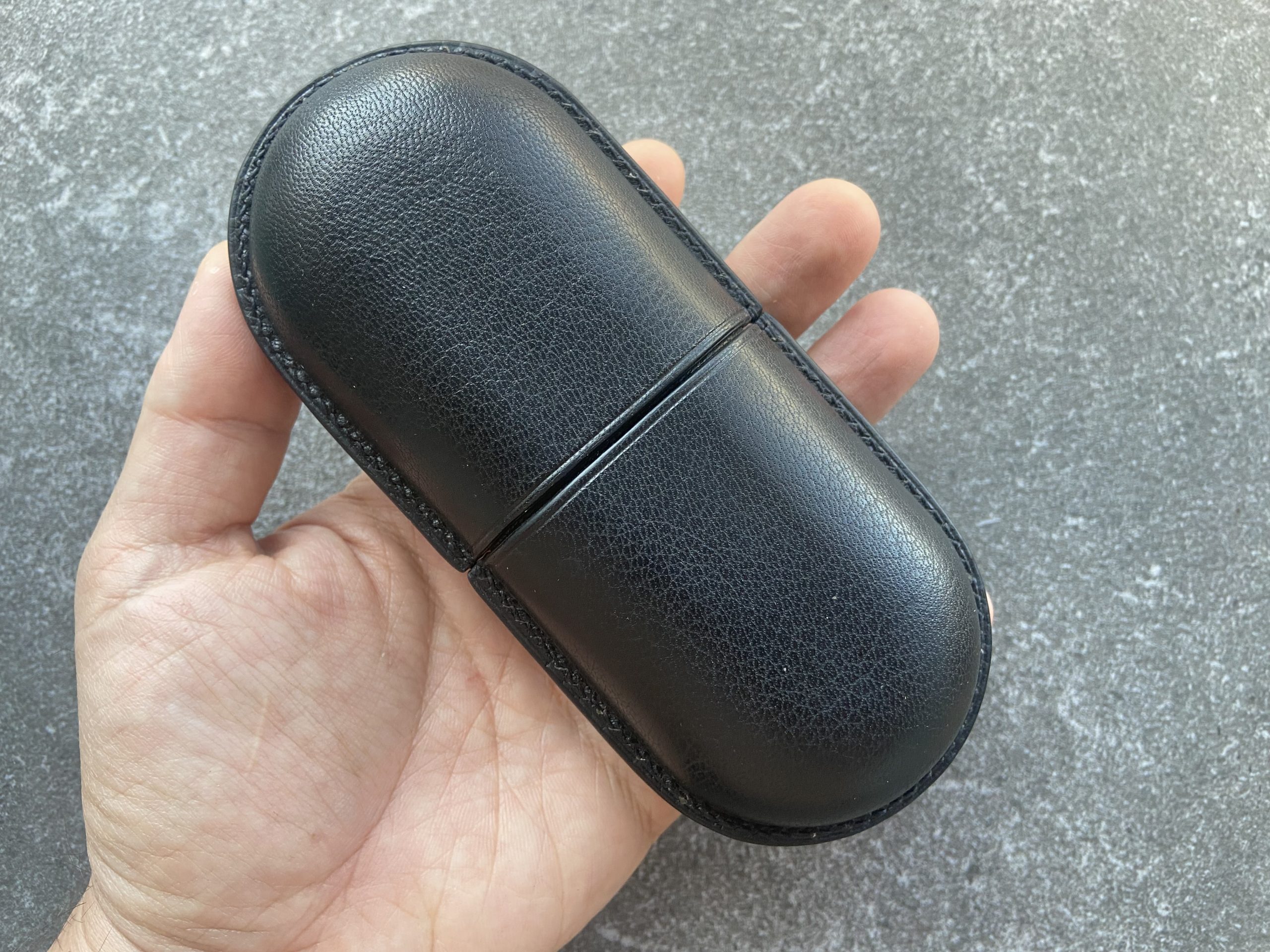 Leather glasses case with sliding lid in black held in hand on a stone surface