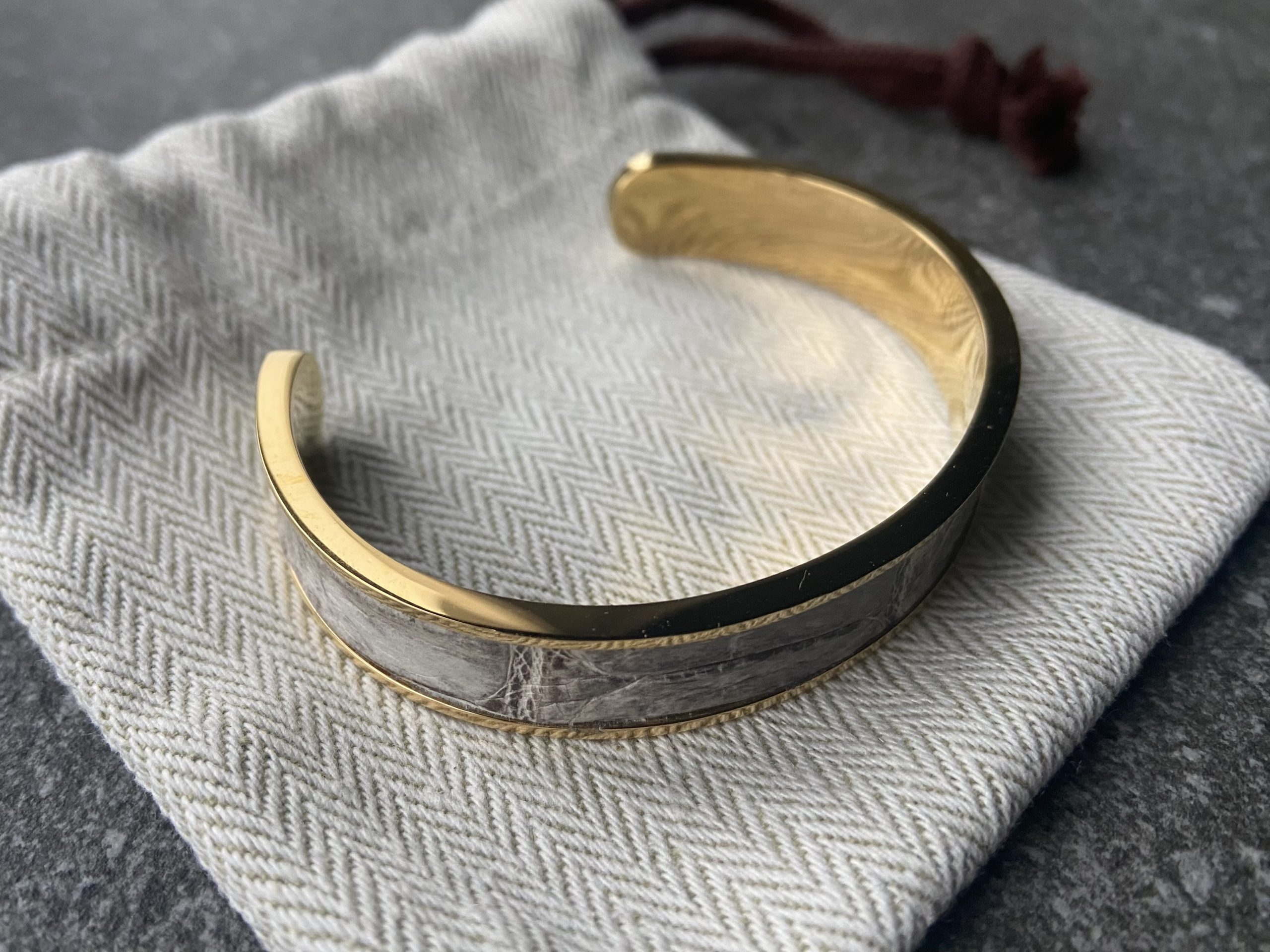 Narrow gold-plated stainless steel cuff bracelet with Himalaya leather inlay on a herringbone fabric pouch
