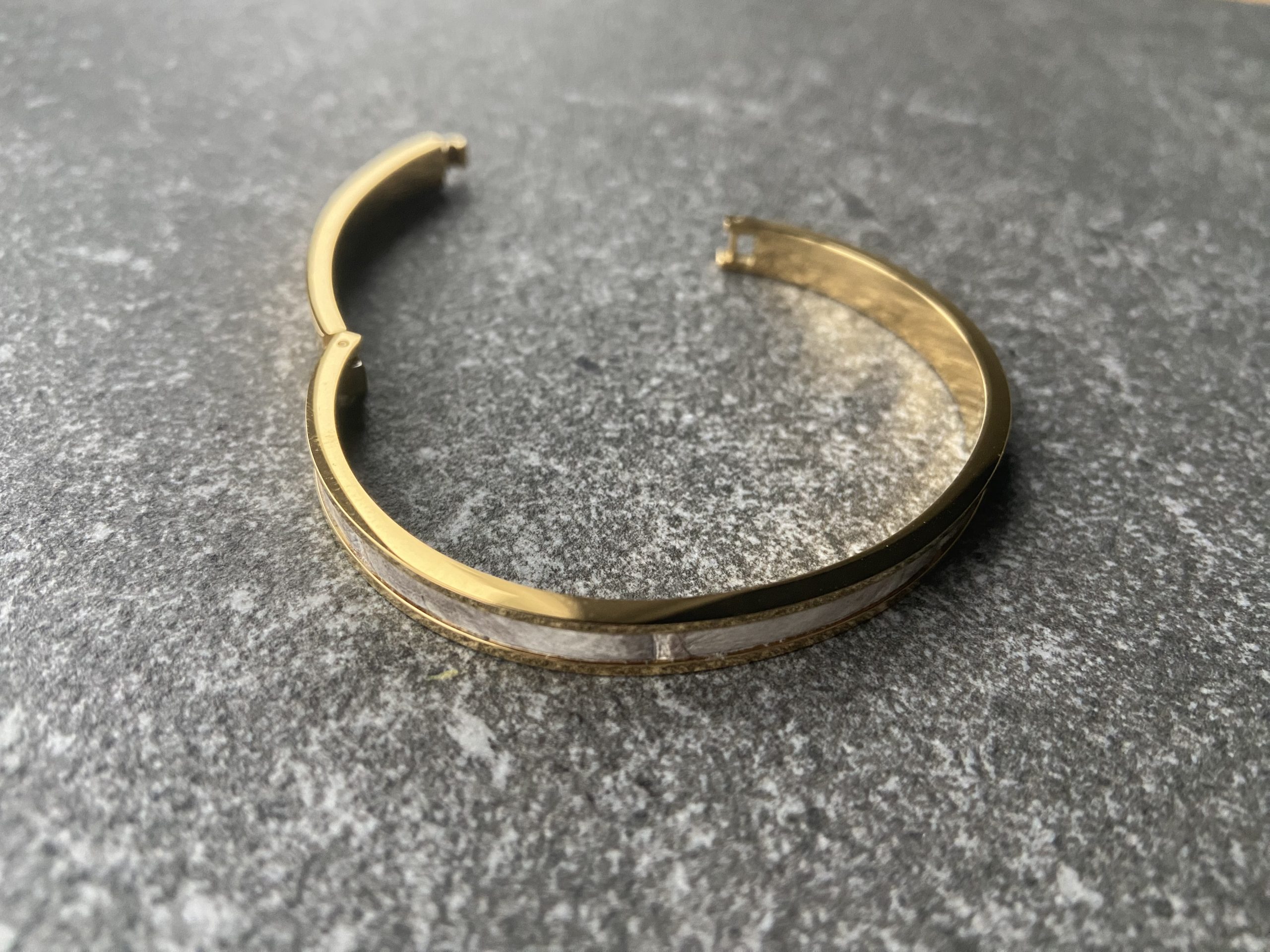 Gold-plated stainless steel clic bracelet with Himalaya leather inlay, open view on stone background