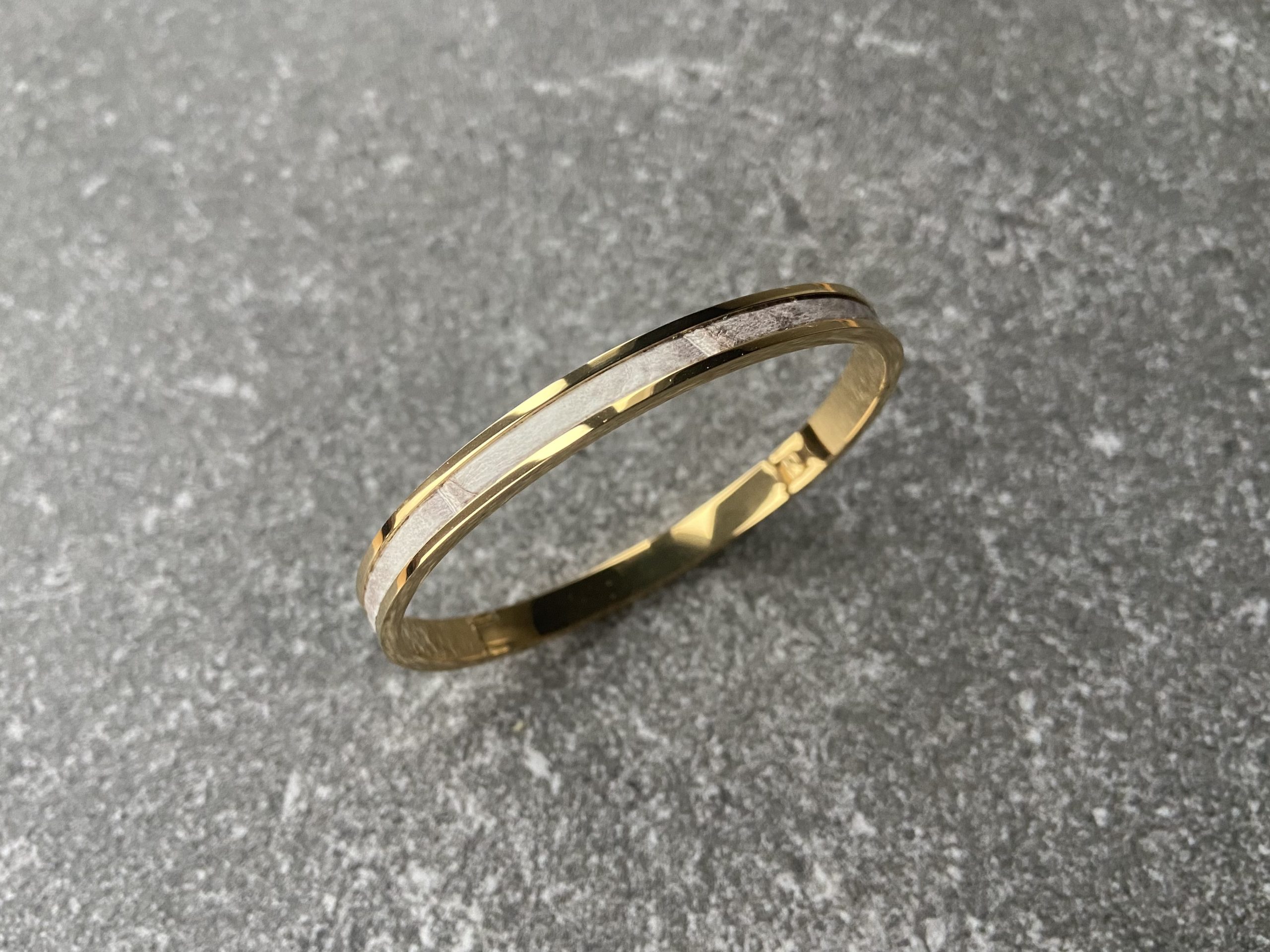Gold-plated stainless steel clic bracelet with Himalaya leather inlay on grey stone background
