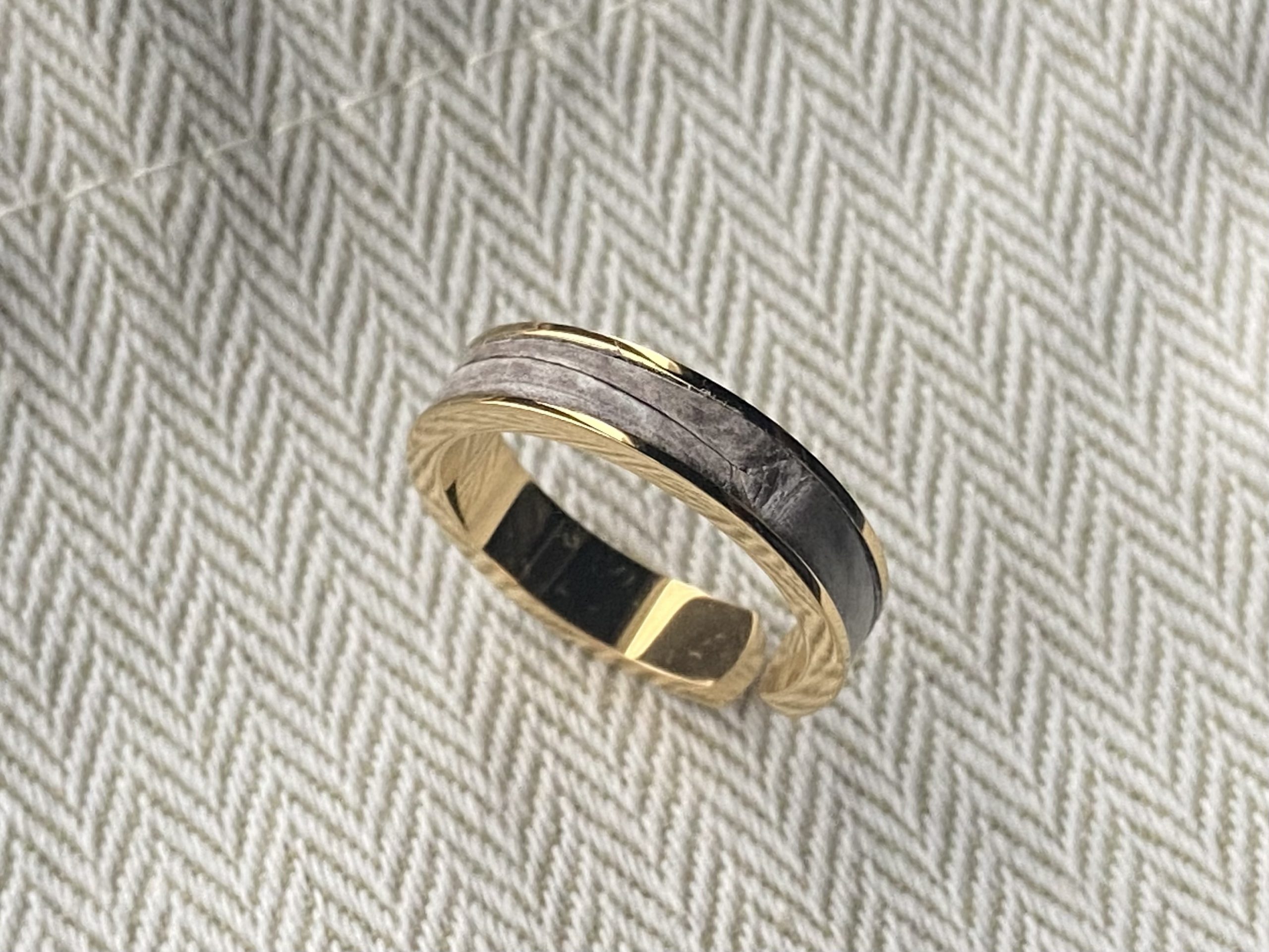 Gold-plated stainless steel ring with Himalaya leather inlay on herringbone fabric, angled view