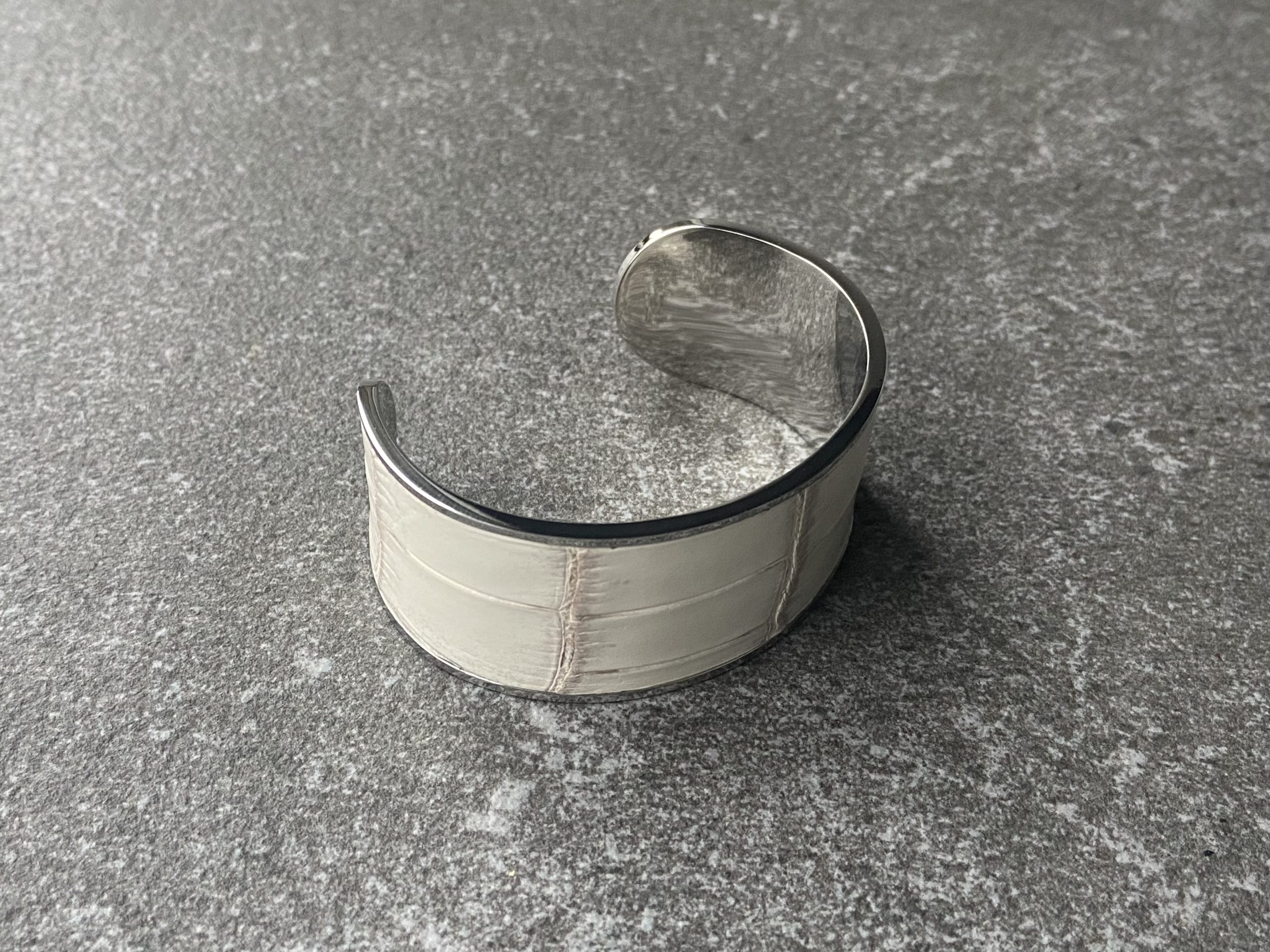Wide stainless steel cuff bracelet with Himalaya leather inlay on a grey stone background, side view