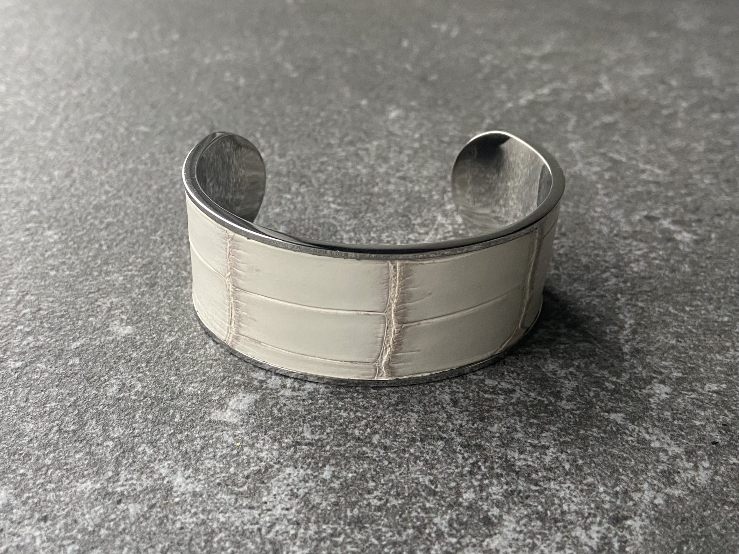 Wide stainless steel cuff bracelet with Himalaya leather inlay on a grey stone background