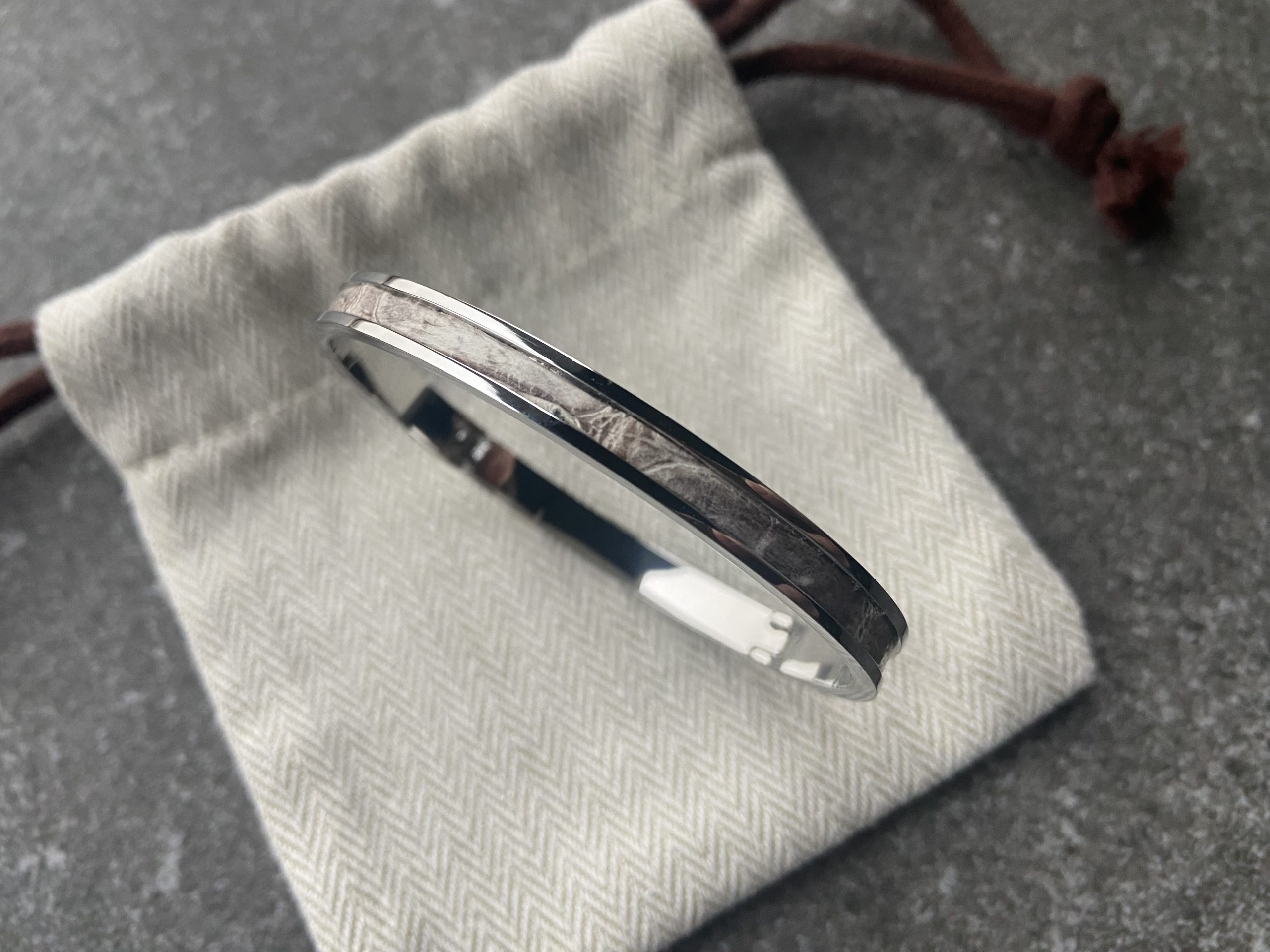 Stainless steel clic bracelet with Himalaya leather inlay resting on a herringbone fabric pouch