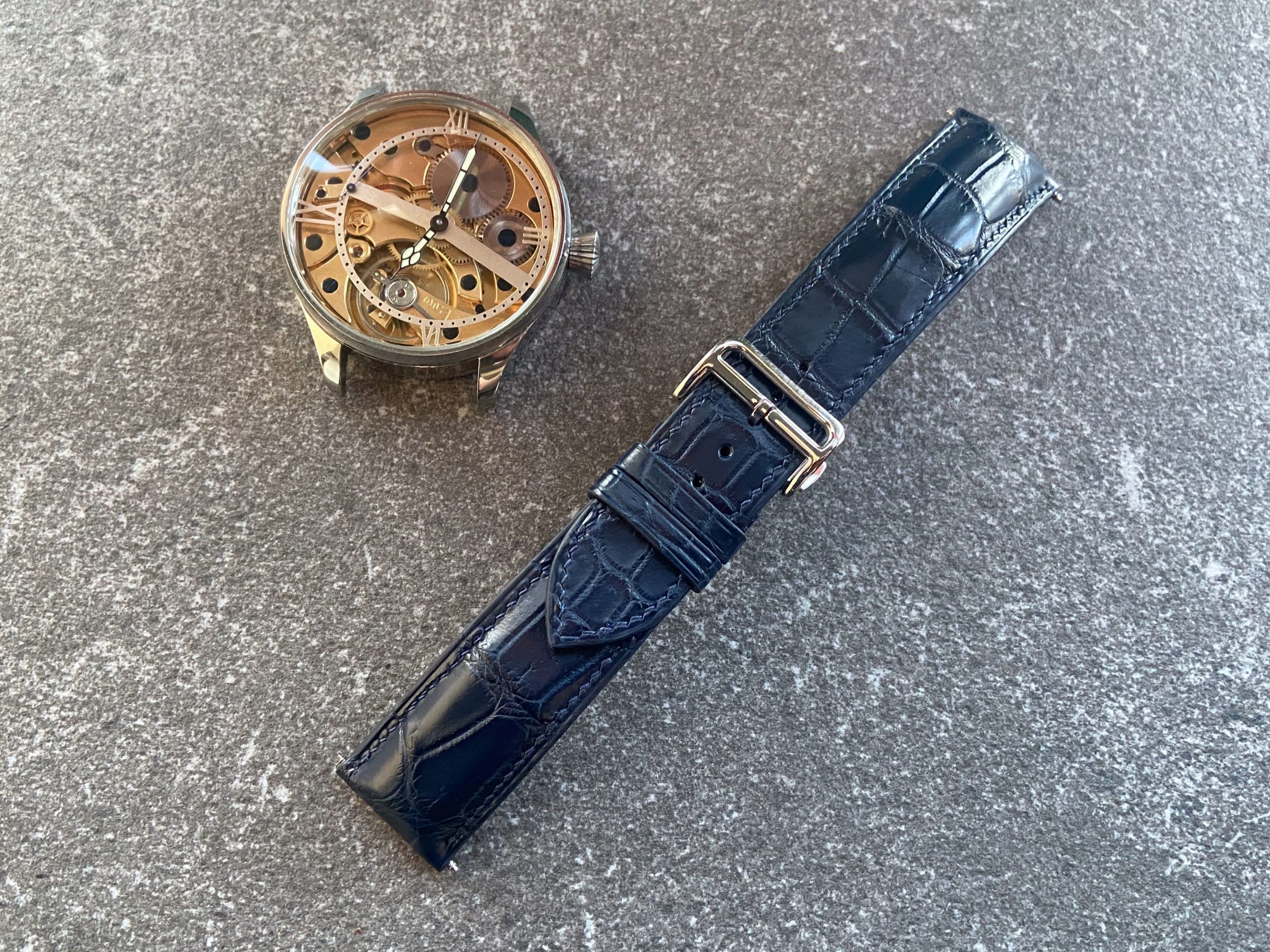 ark blue alligator watch strap next to a skeletonized wristwatch case made from a reversed pocket watch movement