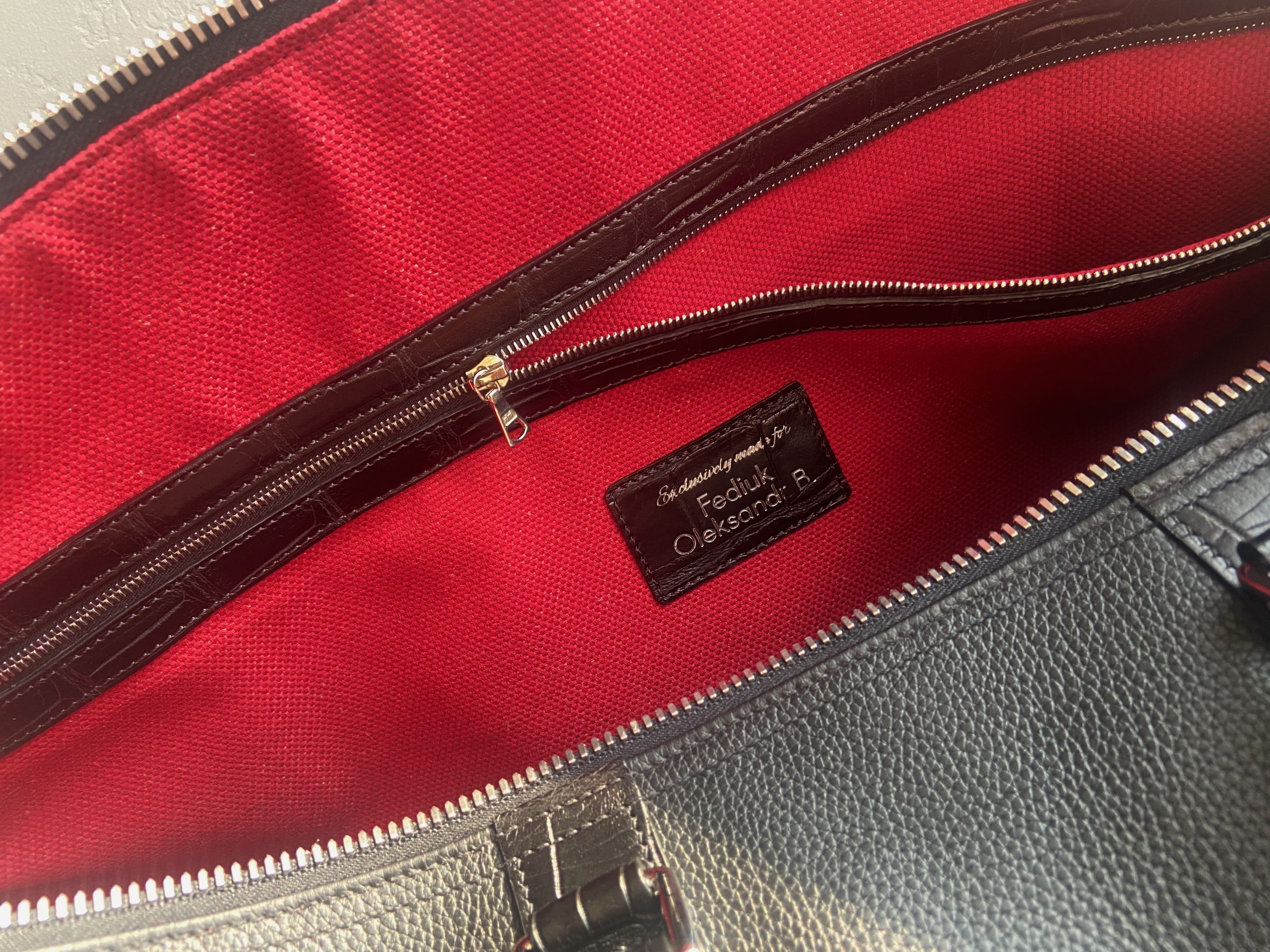 Interior view of the bespoke travel bag showing red lining, alligator-trimmed zip pocket, and personalized name tag
