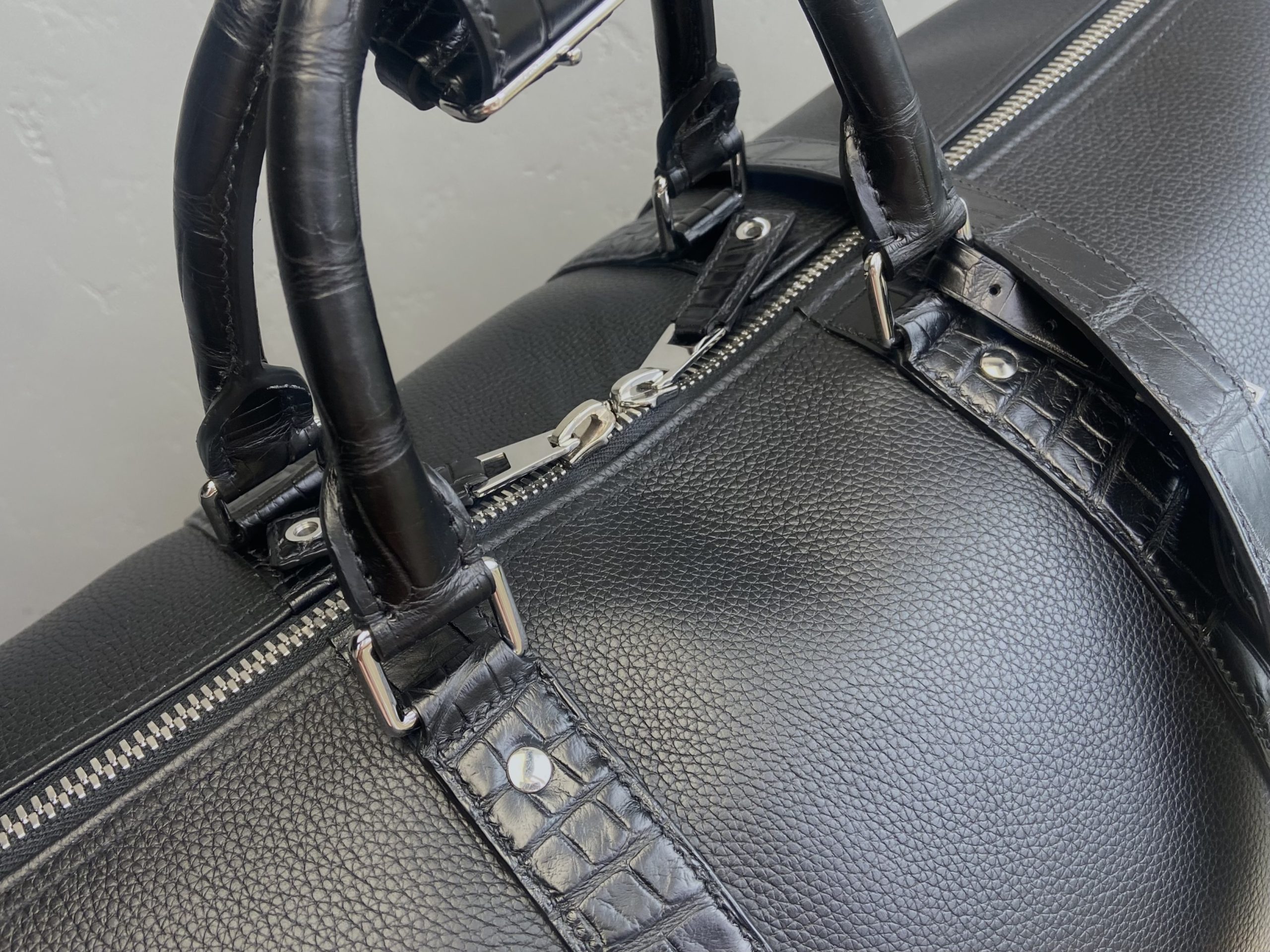 Close-up of the handles and zipper area on a bespoke travel bag in calfskin and alligator leather