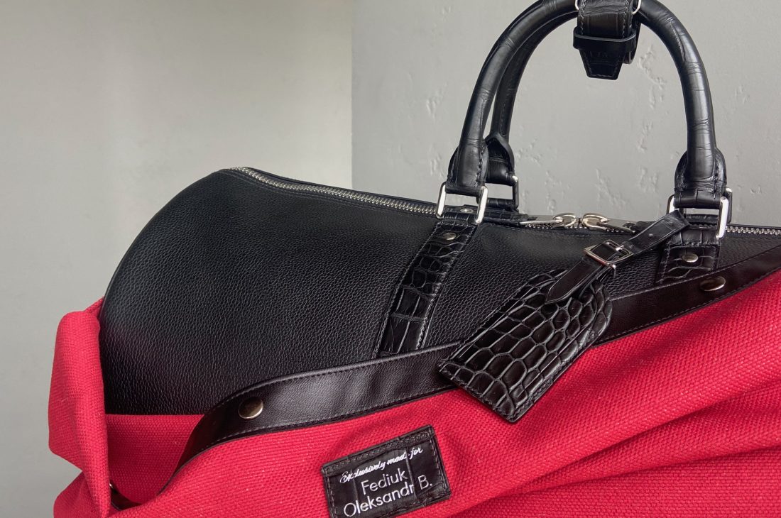 Close-up of the handles, alligator luggage tag, and personalized protective cover on a bespoke travel bag