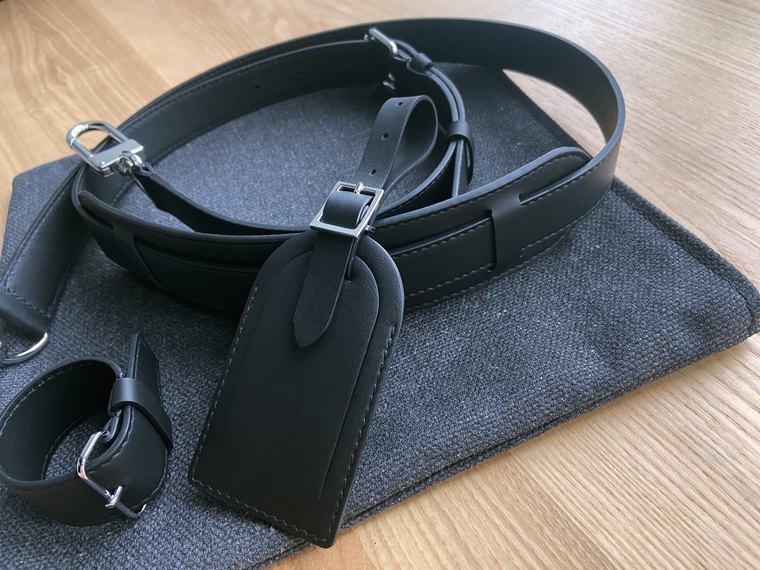 Black leather accessories set including shoulder strap, luggage tag, and handle keeper on dark textile background