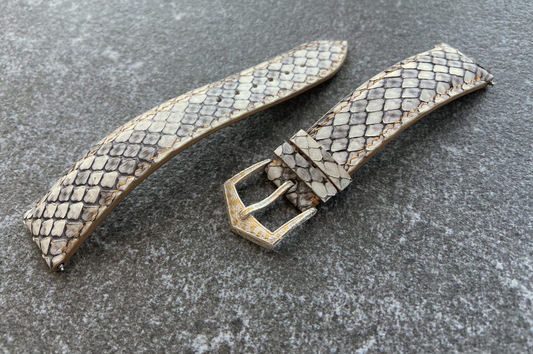 Handmade python leather watch strap with sculpted buckle on gray surface