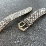 Handmade python leather watch strap with sculpted buckle on gray surface