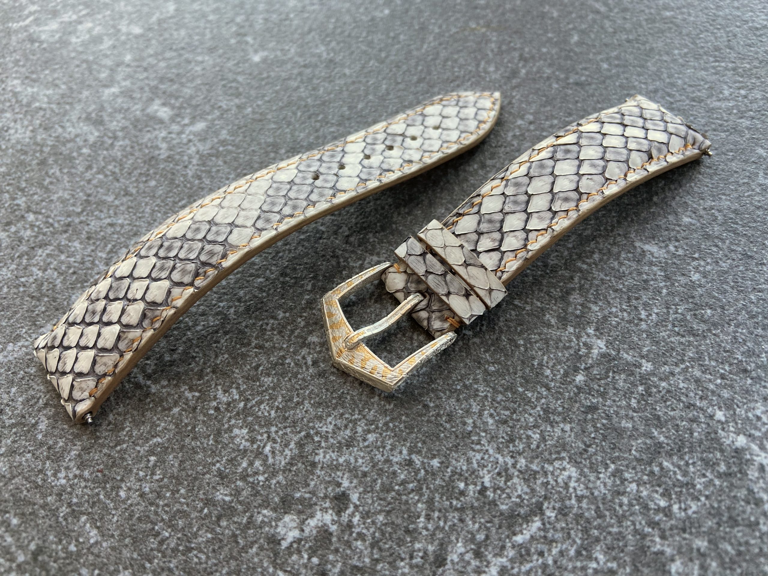 Handmade python leather watch strap with sculpted buckle on gray surface