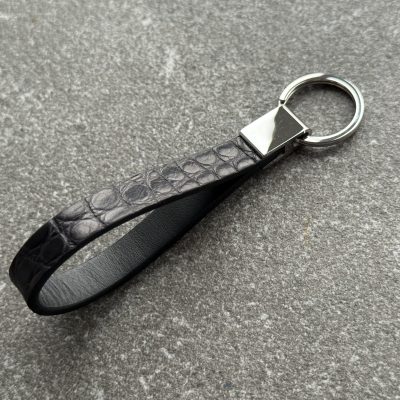 Black structured grain leather loop key holder with polished 316L stainless steel hardware on grey stone surface
