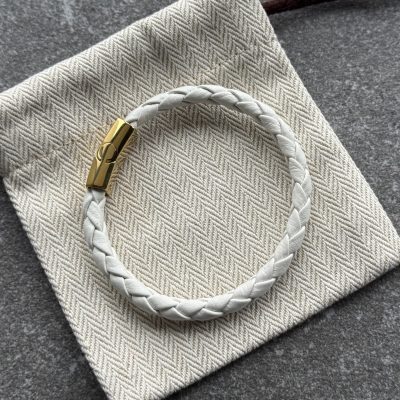 White braided calfskin bracelet with gold clasp on herringbone fabric pouch