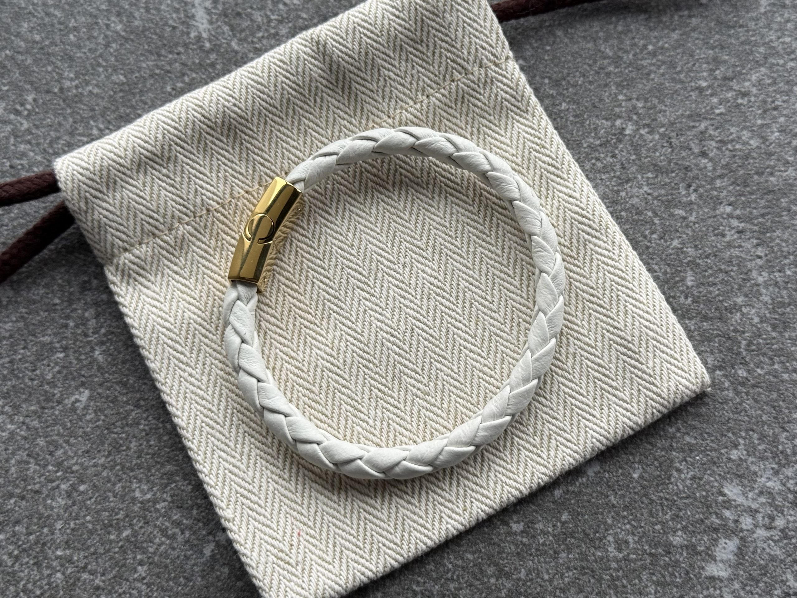 White braided calfskin bracelet with gold clasp on herringbone fabric pouch