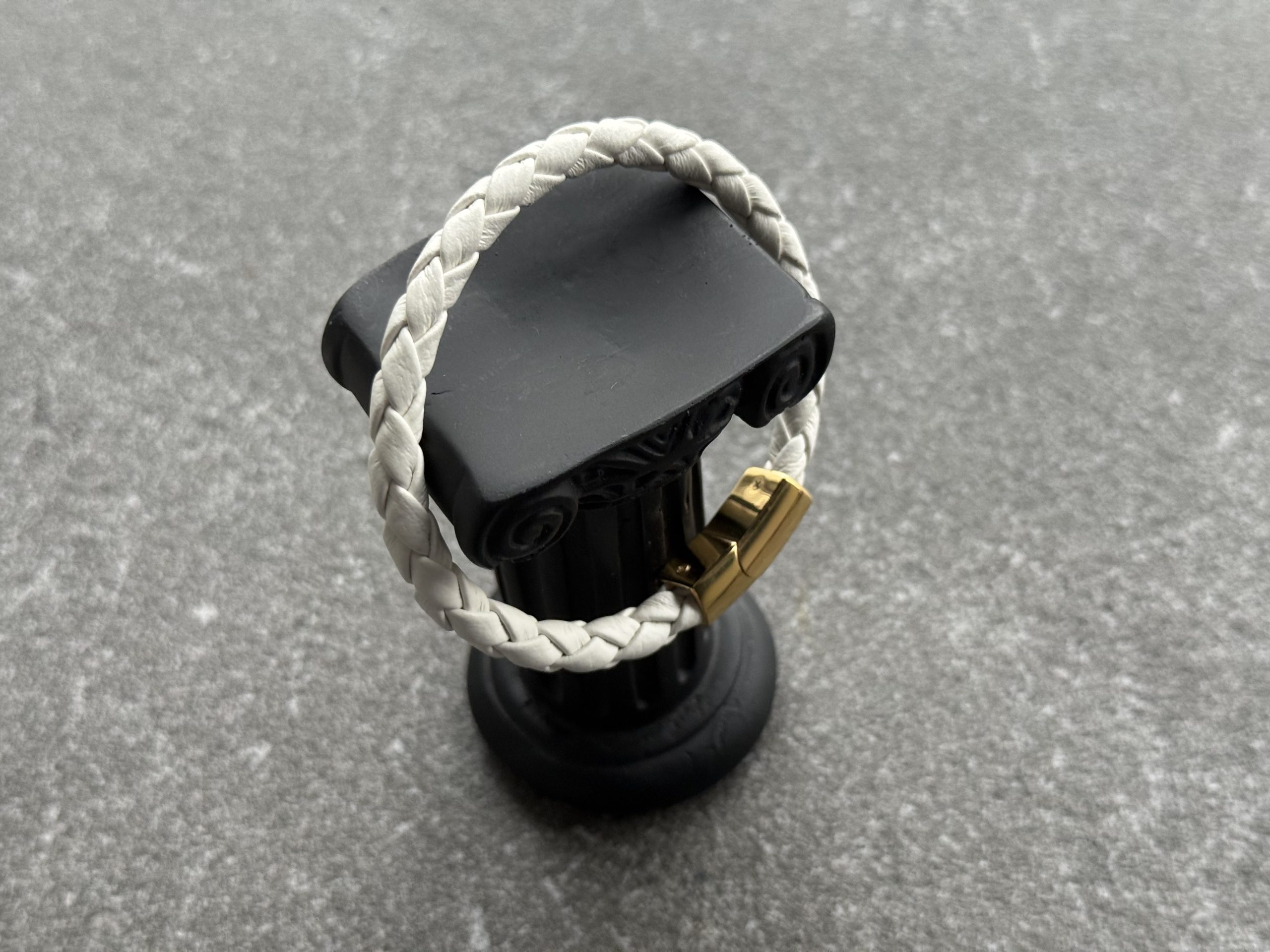 White braided calfskin bracelet displayed on a black column stand