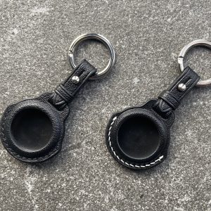 Leather keychains for Apple AirTag with black and white stitching on a stone surface