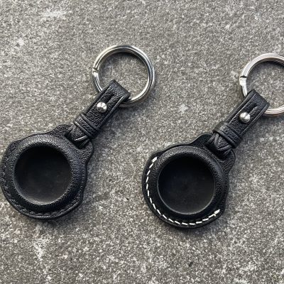 Leather keychains for Apple AirTag with black and white stitching on a stone surface