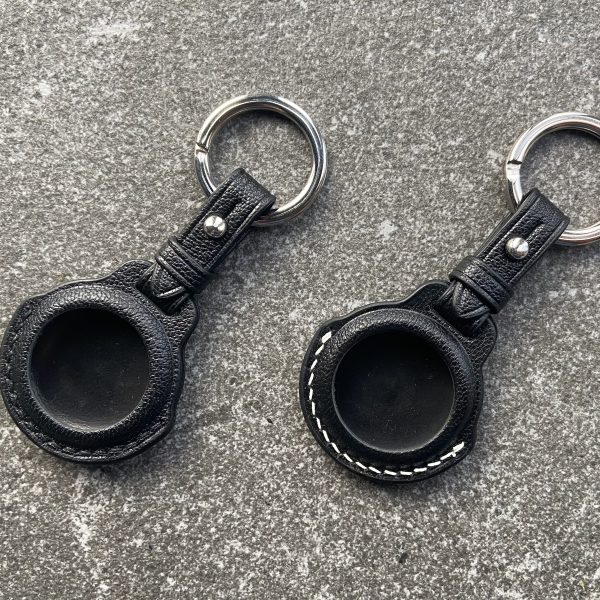 Leather keychains for Apple AirTag with black and white stitching on a stone surface