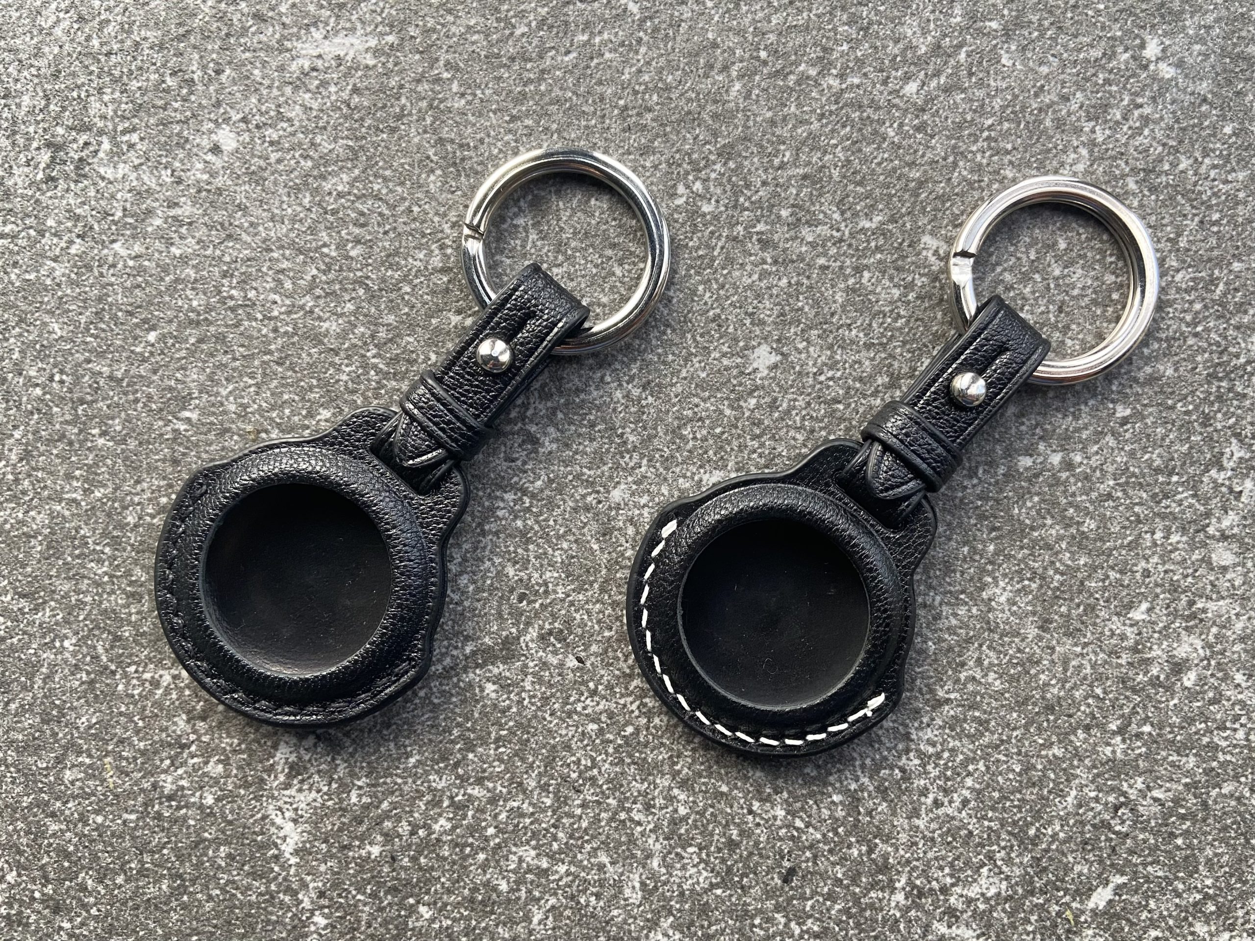 Leather keychains for Apple AirTag with black and white stitching on a stone surface